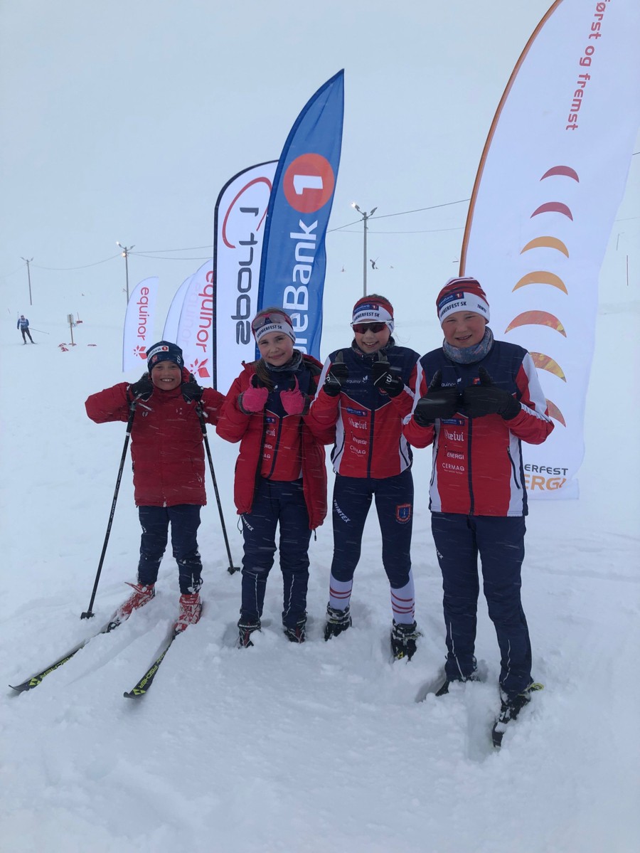 Foto av fire yngre klubbmedlemmer på med skiløype i bakgrunnen
